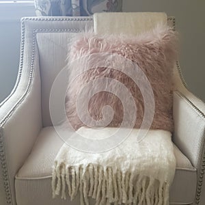 Square Pink furry throw pillow and soft white blanket on armchair inside a bedroom