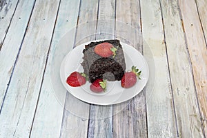 Square portion of moist chocolate cake with strawberries on white plate