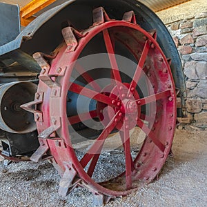 Square Red wheel rim of an and vintage tractor against stone wall of a farm barn