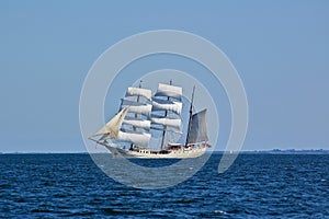 Square-rigged white sailing ship at sea with a distant shore in the background