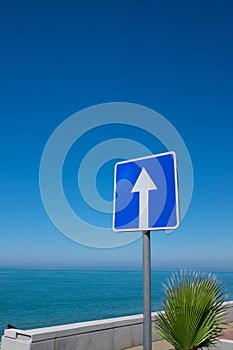 Square road sign with white arrow on blue sky background.