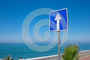 Square road sign with white arrow on blue sky background.