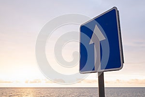 Square road sign with white arrow on blue sky background.