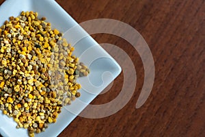 Square saucer full of bee pollen on a dark wooden table