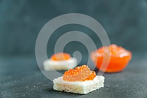 Square shaped sandwich eith red caviar on gray background