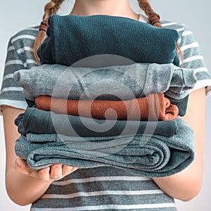 Square shot of a Girl teenager with two braids holding a pile of clothes, isolated on gray background