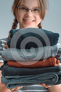 Square shot of young girl holding a pile of clothes, isolated on gray background.