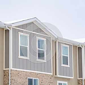 Square Snowy roof brick wall and vertical siding at exterior of townhome against sky
