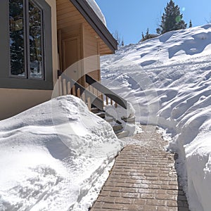 Square Stone brick pathway and stairs leading to home entrance amid deep layer of snow