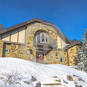 Square Stone home with small balcony over front door decorated with wreath in winter