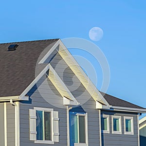 Square Sunlit home with dark pitched roof over horizontal gray wall siding and windows