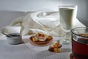 Square toasted pieces of homemade delicious rusk, hardtack, Dryasdust, zwieback, Liquid honey in a saucer, glass of milk and black