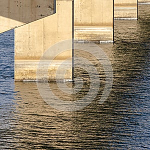 Square Views underneath a beam bridge with abutments against the sunlit lake water