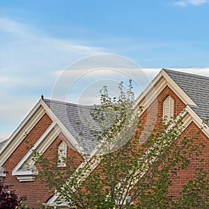 Square Weather vane and vent on top of the gray gable roof of home against blue sky