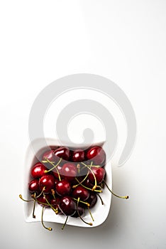 Square white bowl of fresh red cherries on white background. Isolated plate with berries and copy space for text. Ripe sweet berri