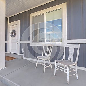 Square White porch chairs against window and front door of home with gray exterior wall