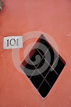 Square window in pink wall whit civic number