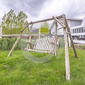 Square Wooden bench swing at the lush grassy yard of a home with white picket fence