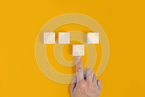A square wooden block is placed on a yellow background, the hand is pushing the third wooden block into place. Wood block concept photo