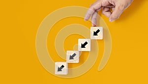 A square wooden block is placed on a yellow background, on the wooden block showing a down arrow and a hand doing a downward photo