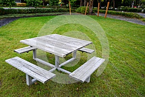 Square wooden picnic table with four benches, on a rain-soaked lawn