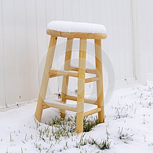 Square Wooden stool on snow covered ground in winter against white wood fence