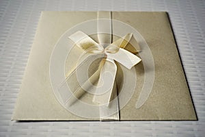 Squared silver envelope with pearly ribbon and topknot as an example of typical wedding invitation and wedding announcement cover