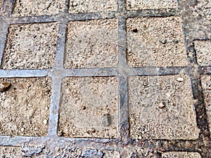 Squares in a metal grid lying on concrete, pebbles, earth. The old sidewalk or wall. A pattern of metal rods. Background