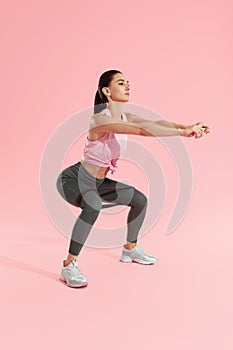 Squats. Woman in sports wear squatting with resistance band