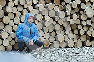 Squatting lumberjack at stack of logged firewood background outdoors in winter mountain forest