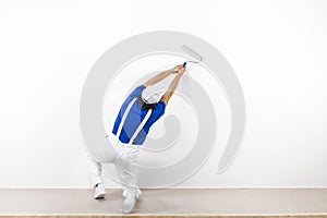 Squatting painter with paintroller on white wall photo