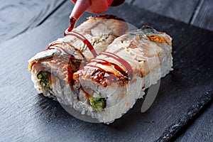 Squeeze brown sauce on a set of sushi rolls with cream cheese, rice and salmon on a black board decorated with ginger and wassabi