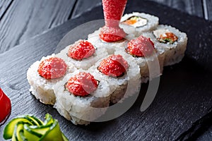 Squeeze red sauce on a set of sushi rolls with cream cheese, rice and salmon on a black board decorated with ginger and wassabi on