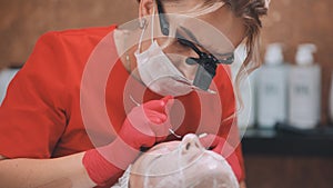 Squeezing acne from a girl with problem skin in the salon using a loop.