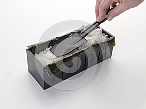 Squeezing rice with a spatula inside a cut box for makis photo