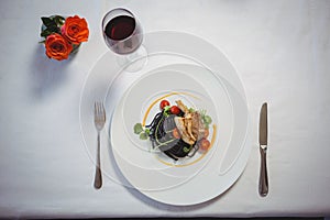 Squid ink spaghetti dish with basil with flowers and red wine