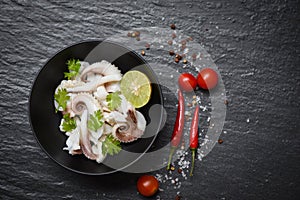 Squid salad bowl with lemon herbs and spices on dark background top view - Tentacles octopus cooked appetizer food hot and spicy