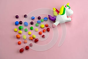 squishy toy unicorn is flying on a candies rainbow on pink background