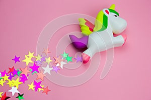 squishy toy unicorn and glitters in the shape of stars on pastel pink background