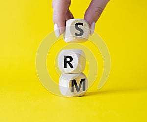 SRM - Sustainability Risk Management symbol. Wooden cubes with word SRM. Businessman hand. Beautiful yellow background. Business