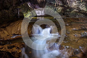 St. Beatus Cave and waterfalls above Thunersee, Sundlauenen, Switzerland. Falls are running down the mountain with a green grass