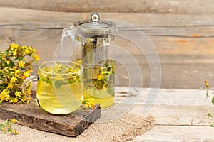 St. John's wort tea is a therapeutic healthy drink, a teapot and a cup on a wooden background, a bouquet of St