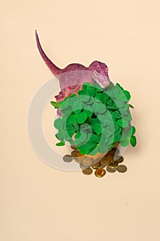 St. Patrick's Day happy dinosaur, a bouquet of clover in a bucket and gold coins on a beige background. Vertical