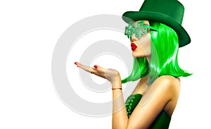 St. Patrick`s Day leprechaun model girl in green hat, funny clover sunglasses holding product, pointing hand, isolated on white