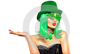 St. Patrick`s Day leprechaun model girl in green hat, funny clover sunglasses holding product, pointing hand, isolated on white