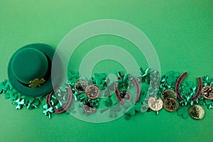 St Patricks Day border of shamrocks and gold coins and horseshoe over a green background. Top view, flat lay.