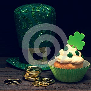 St. Patricks Day Cupcake decorated with Shamrocks and gold coins, and top hat on Dark Rustic Wood Table and Background with copy s