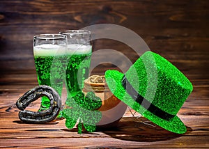 St Patricks day with glasses of green beer, leaf clover, leprechaun hat, horseshoe and pot full gold coins on vintage wooden back