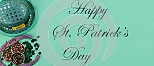 St Patricks day holiday celebration with Irish elf hat, horse shoe, gold and clovers on a green paper background plus text