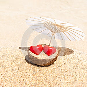 St. Valentine Day and February 14th greeting card. Two red hearts - love couple under beach umbrella. Romantic travel